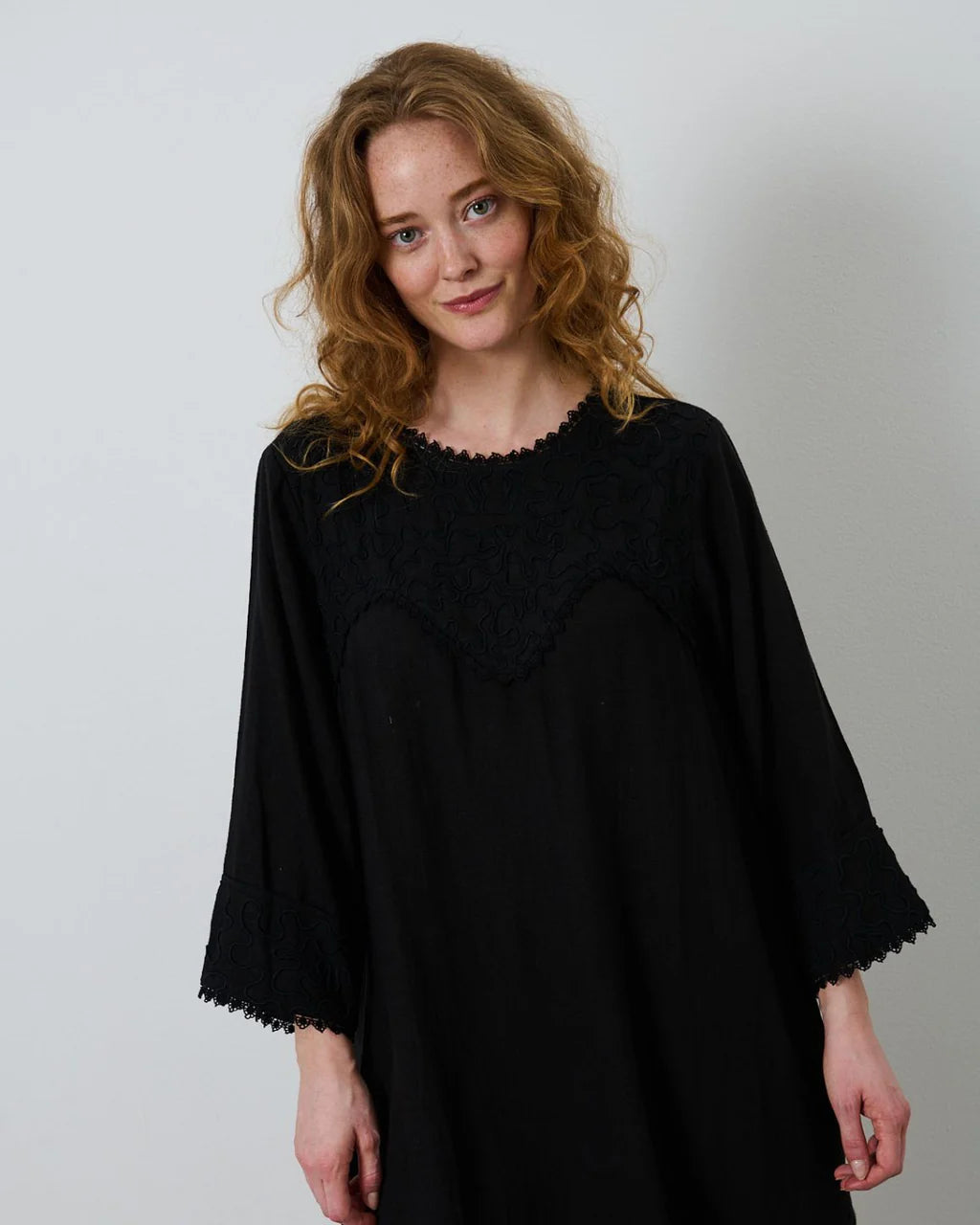 Sort kjole med broderi og blondebånd langs alle kanter.