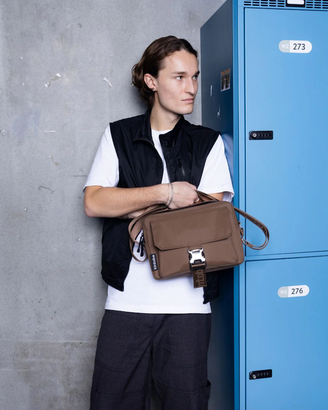 Brun taske med spænde foran, der åbner op til et seperat rum. Ovenpå crossbody'en sidder den vandafvisende lynlås, der åbner til det store rum. Der er en justerbar rem samt et håndtag for oven, så du kan bære den på flere måder.