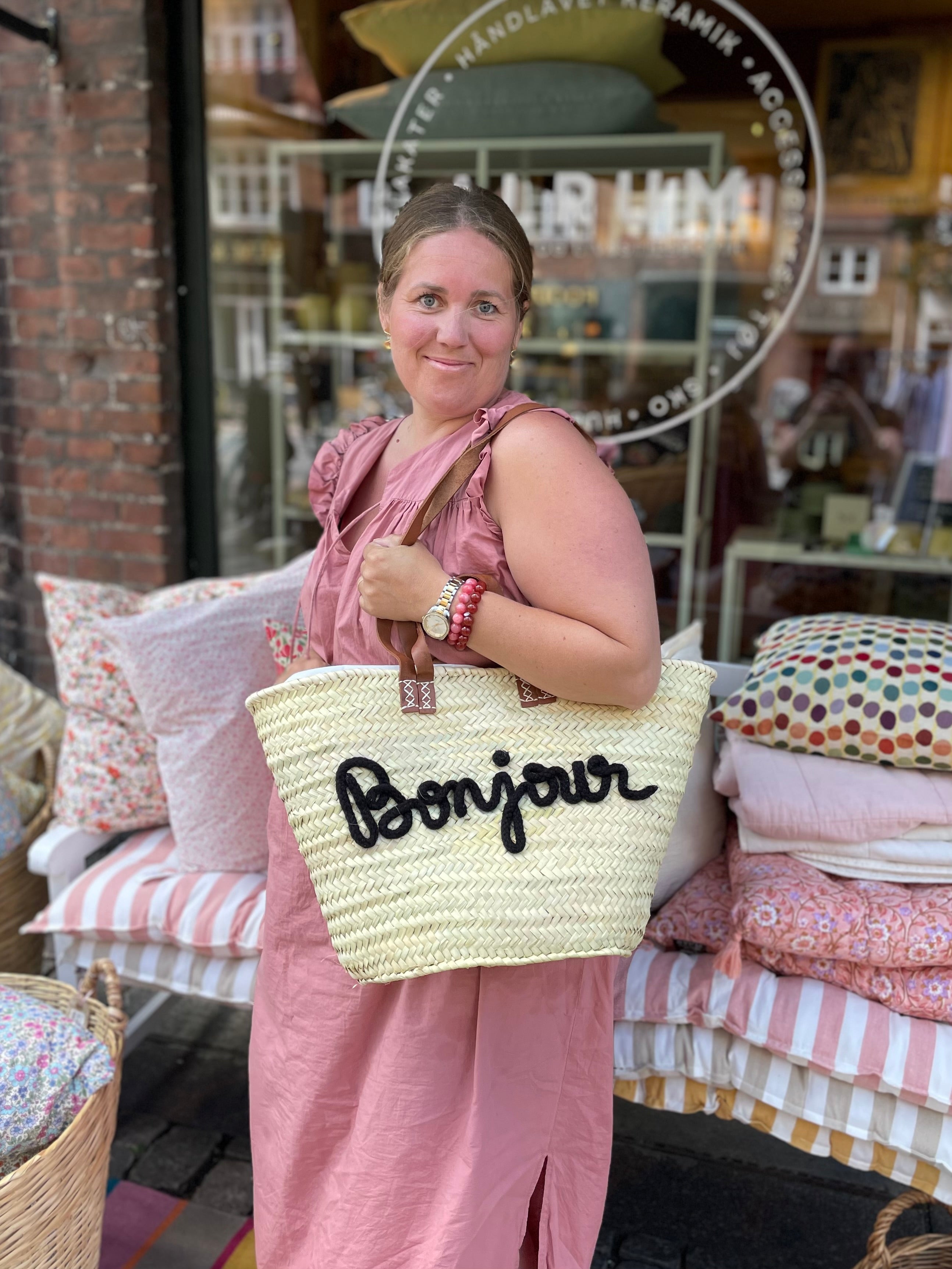 Stor flettaske med brune hanke, sort Bonjour tekst og praktisk lukkepose indeni – køb hos Butik Alrum på Amager eller online på butikalrum.dk.