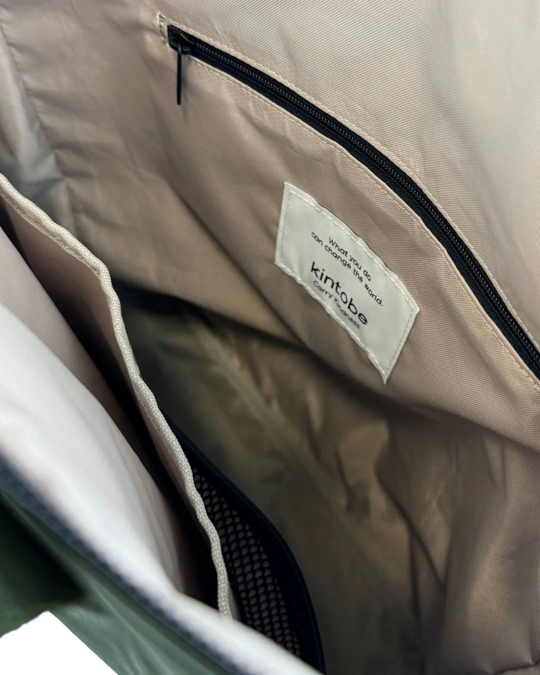 Grøn taske, der kan bruges som tote bag eller rygsæk - og stropper kan skjules. Den har håndtag i toppen, der gør den nem at bære. På toppen sidder lynlåsen, der åbner op til et stort rum med lyst for.