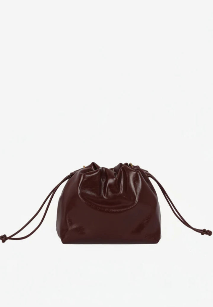 Arcane Raw clutch i Deep Burgundy med justerbar rem, knudedetaljer og magnetisk lukning.