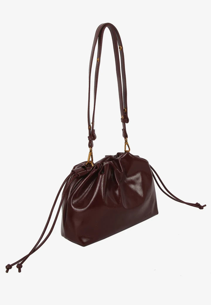 Arcane Raw clutch i Deep Burgundy med justerbar rem, knudedetaljer og magnetisk lukning.