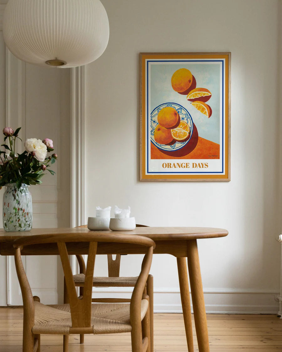 Plakat af intense orange appelsiner, hele og skåret i både. I blå og hvid skål, der står flot i kontrast til de farverige syrlige frugter.