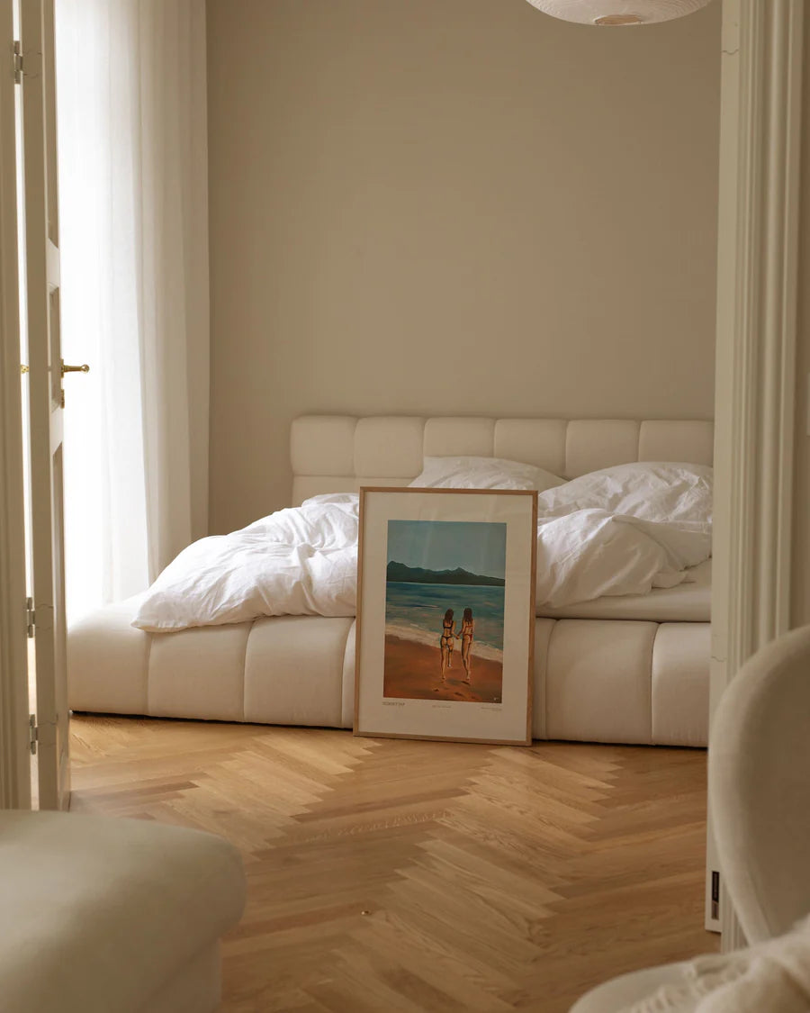 Sunset Dip en plakat, der formidler glade minder. Her to veninder på stranden, der skal i vand med bjerge i baggrunden. Rolige farver, der passer til dig, der vil have en harmonisk plakat til boligen.
